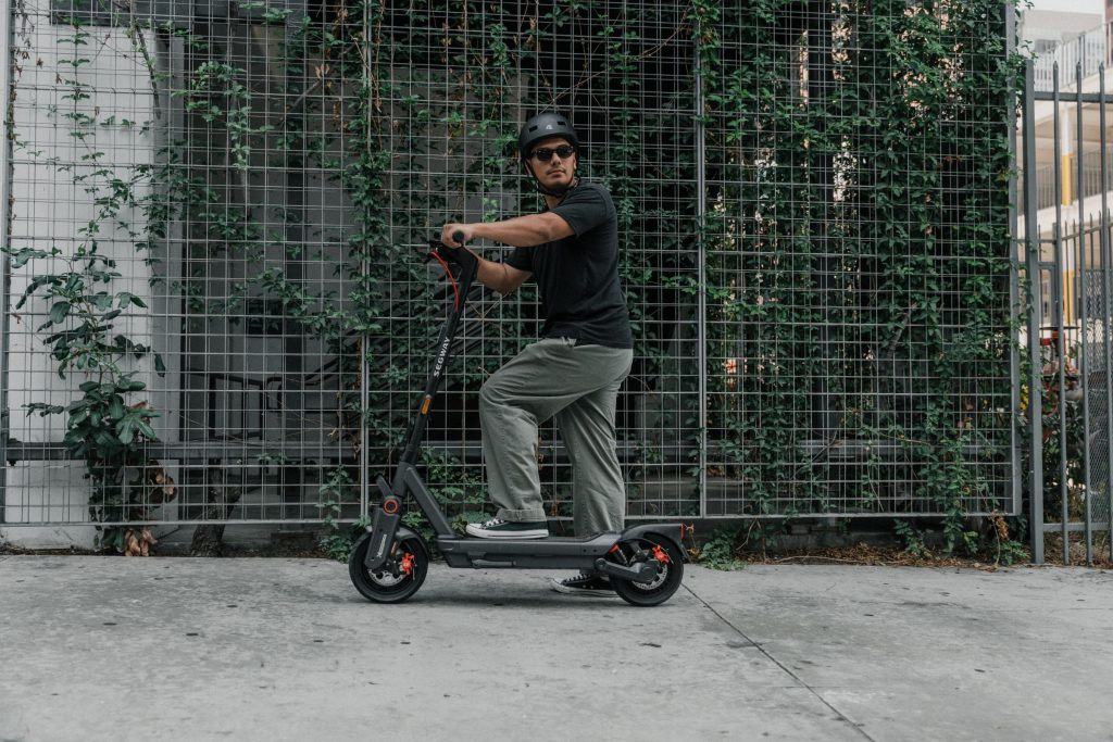 Rider standing with a Segway MAX G3 Plus electric scooter by a green wall