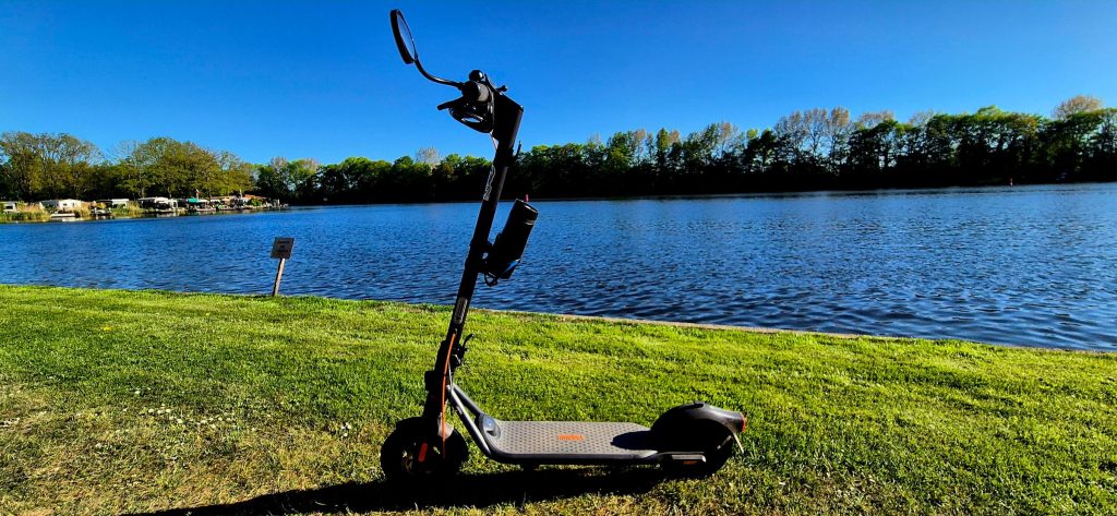 A Segway F2 Pro electric scooter parked on the grass beside a lake.
