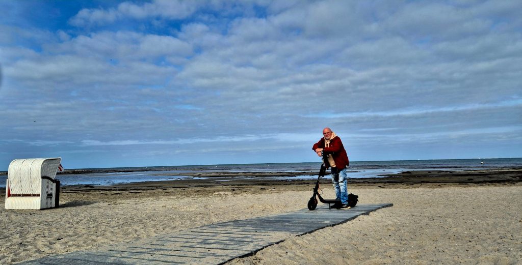 A Segway F2 Pro rider standing with his electric scooter on a path by the sea.