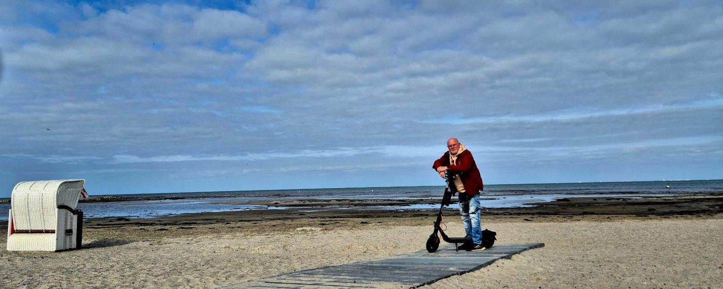 A Segway F2 Pro rider standing with his electric scooter on a path by the sea.