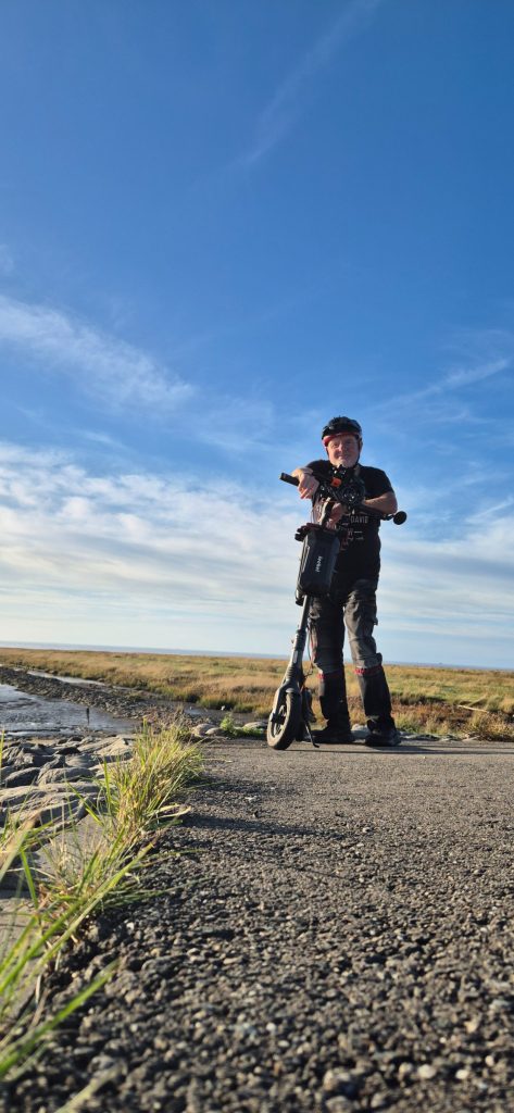 A Segway F2 Pro rider standing with his electric scooter on a coastal path.