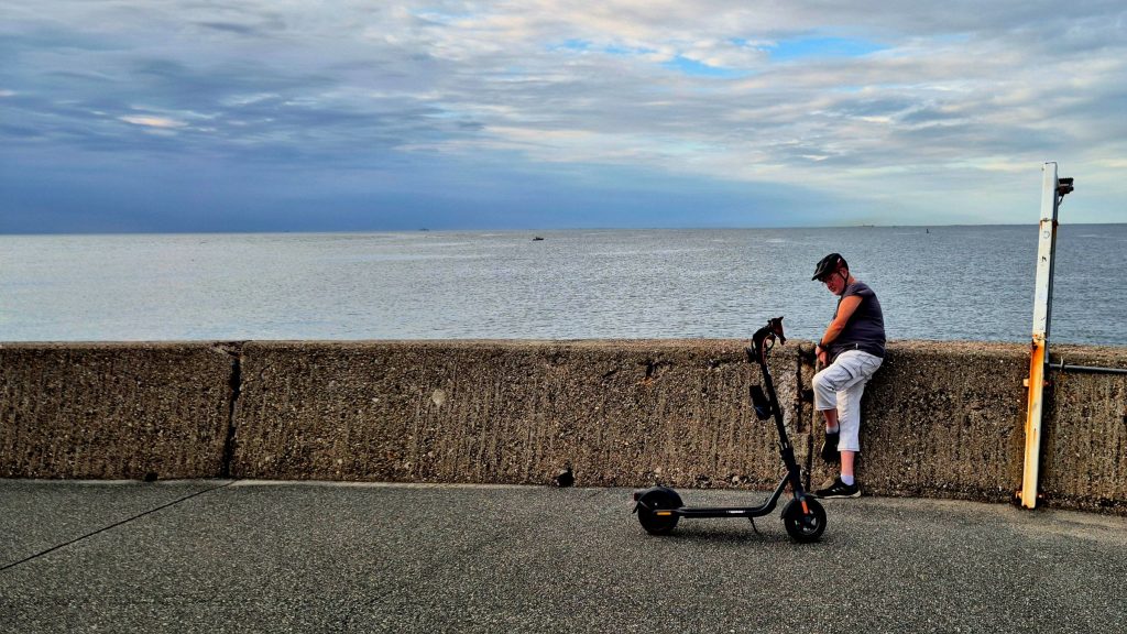 A rider resting on a seawall next to his Segway F2 Pro electric scooter.