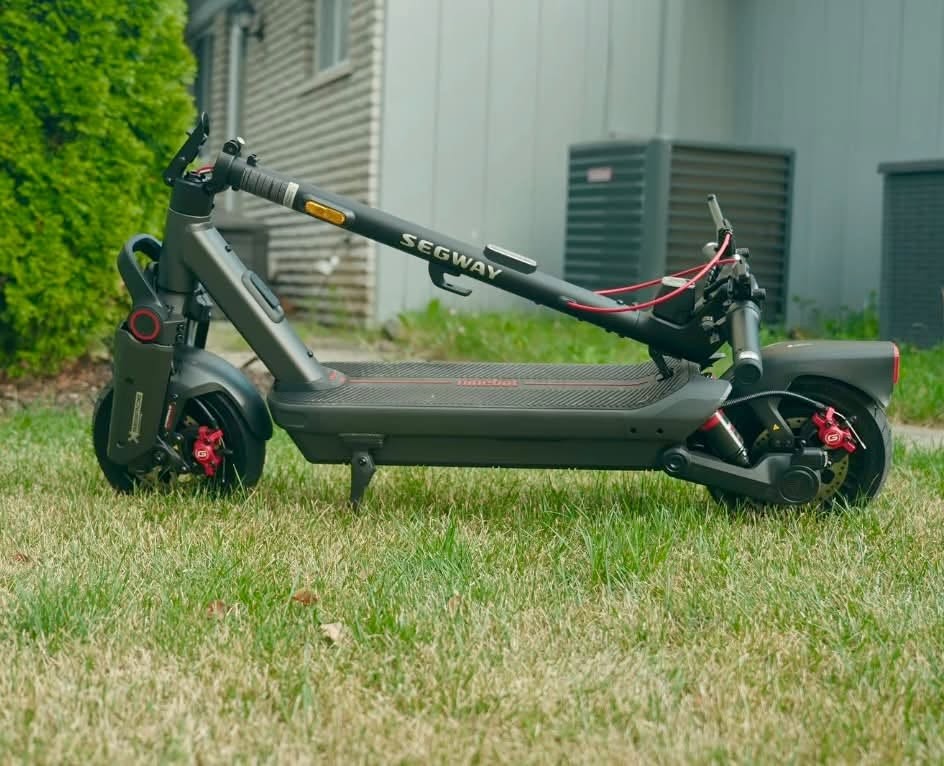 A Segway MAX G3 Plus electric scooter resting on the grass beside a house.