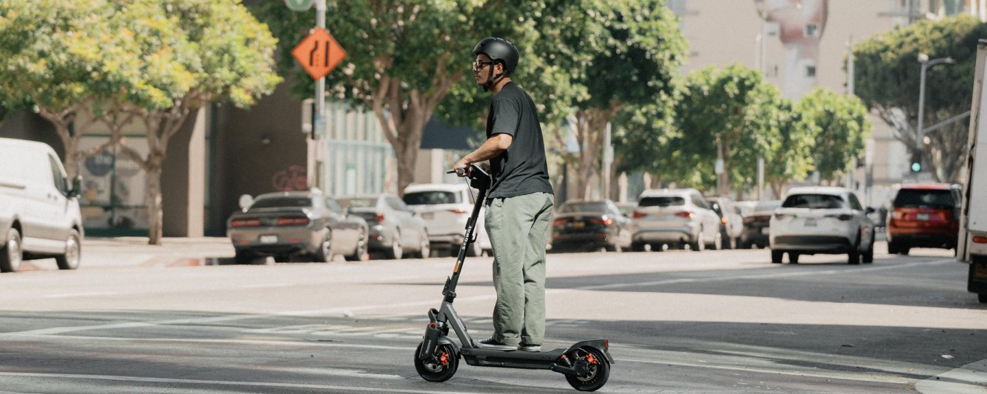 Rider on a Segway MAX G3 Plus electric scooter on a city street lined with parked cars