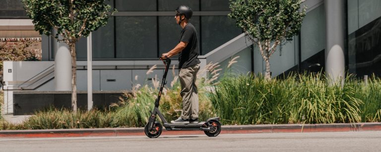 Commuter riding a Segway MAX G3 Plus electric scooter along a landscaped street