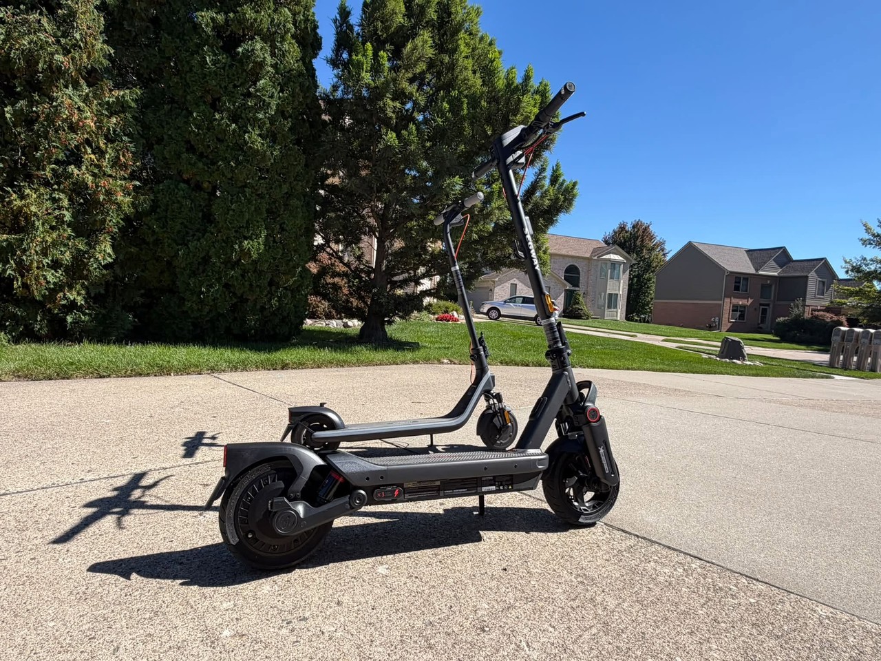 A Segway MAX G3 Plus and a smaller Segway E2 Plus electric scooter parked on a sunny driveway.