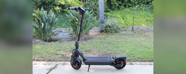 A Segway MAX G3 Plus electric scooter parked on a sidewalk next to a garden.