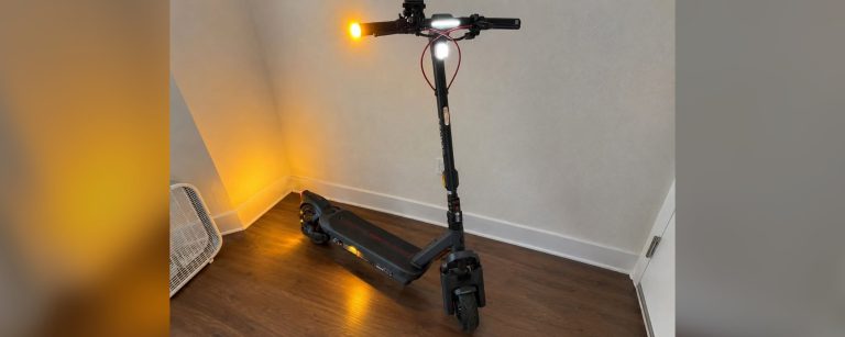 A Segway MAX G3 Plus electric scooter with its lights on, parked in the corner of a room.