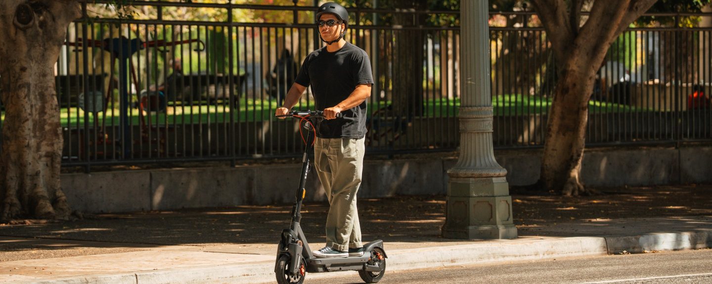 Rider on a Segway MAX G3 Plus electric scooter on a shaded path beside a park