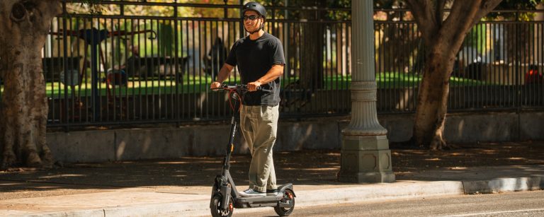 Rider on a Segway MAX G3 Plus electric scooter on a shaded path beside a park