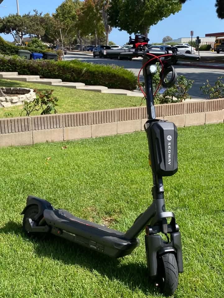 A Segway MAX G3 Plus electric scooter with a handlebar bag standing on a sunny lawn.