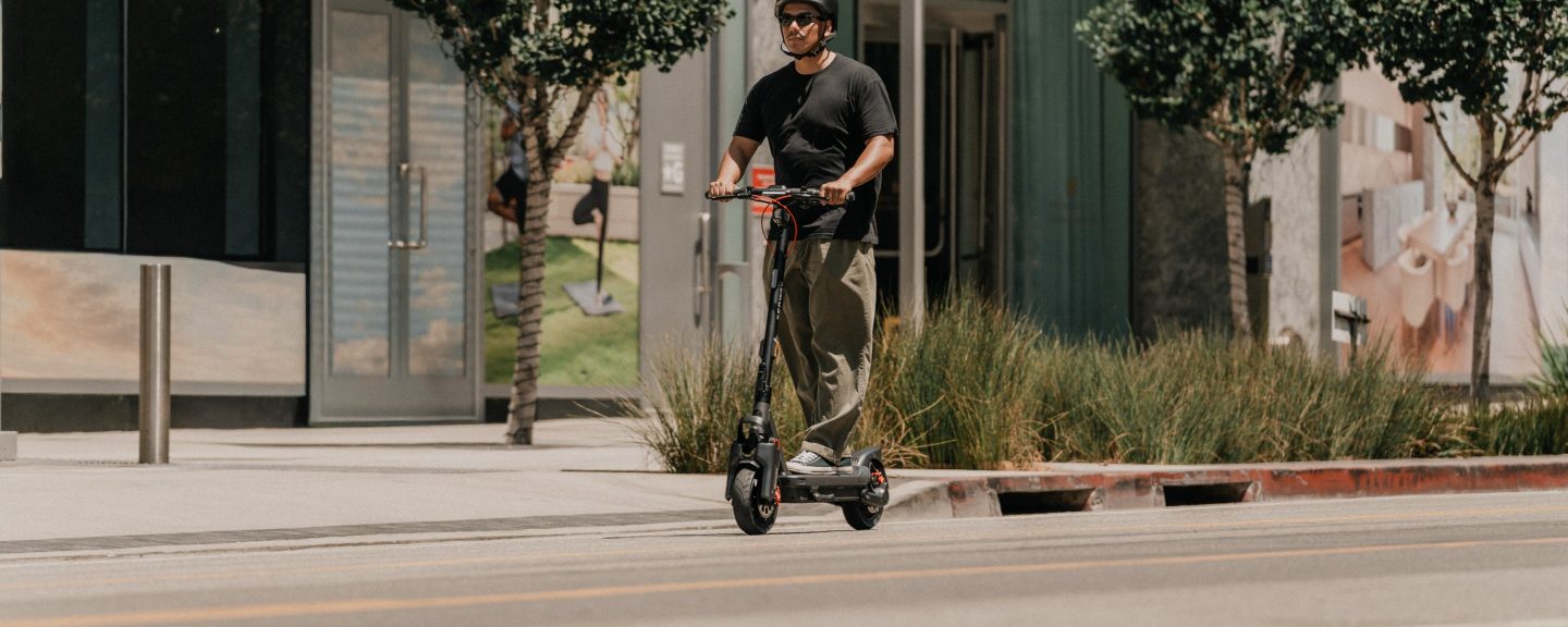Rider on a Segway MAX G3 Plus electric scooter passing a modern building