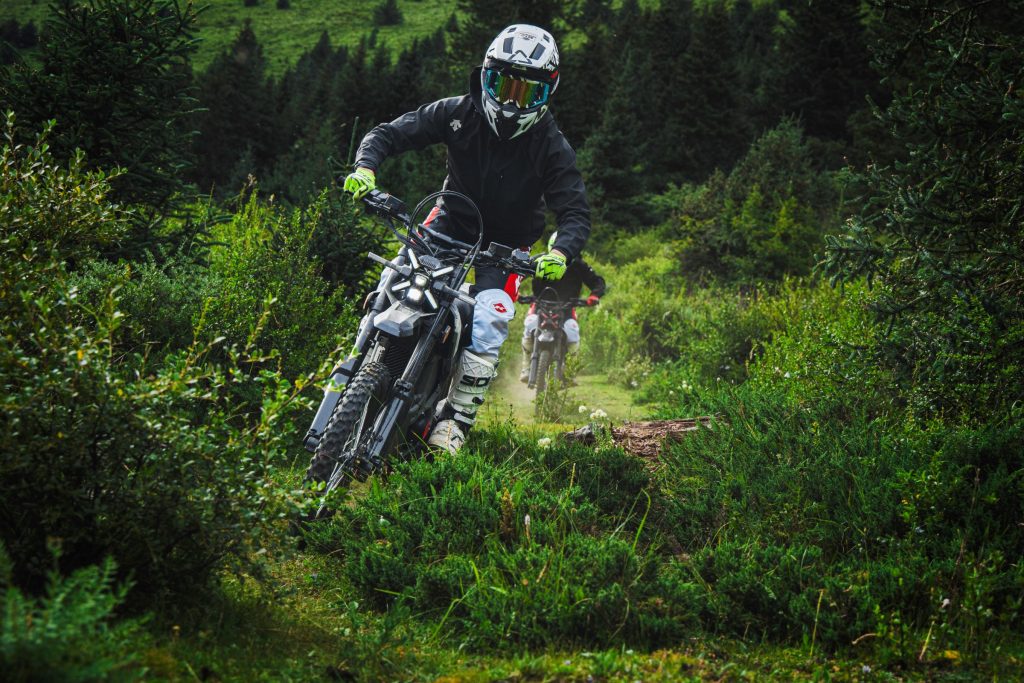Rider on a Segway Xaber 300 electric dirt bike on a green forest trail