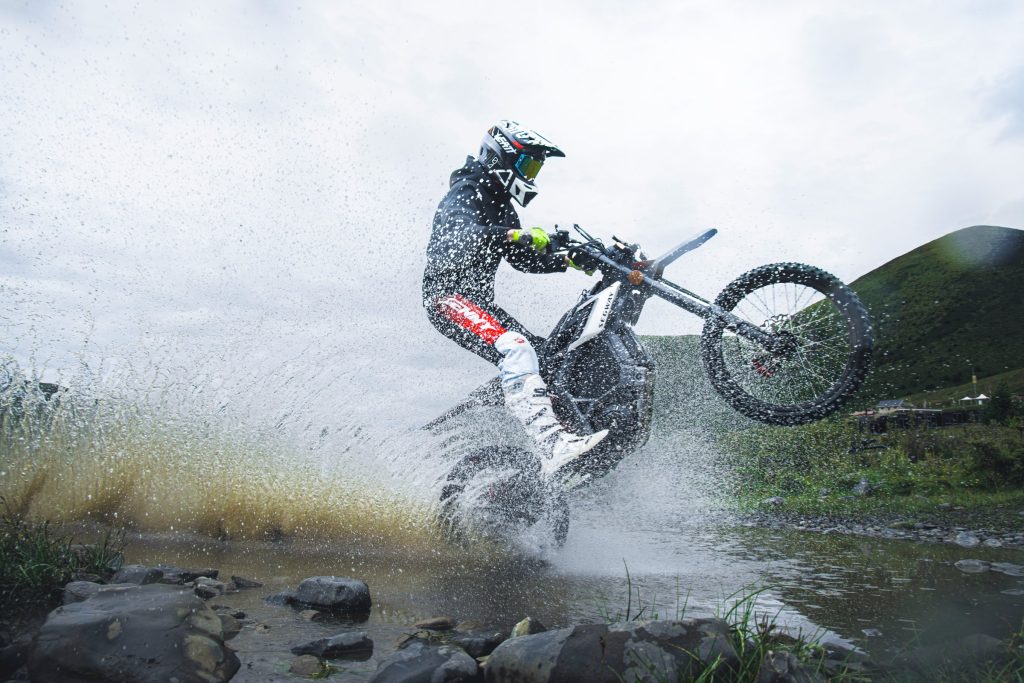 Rider splashing through a stream on a Segway Xaber 300 electric dirt bike