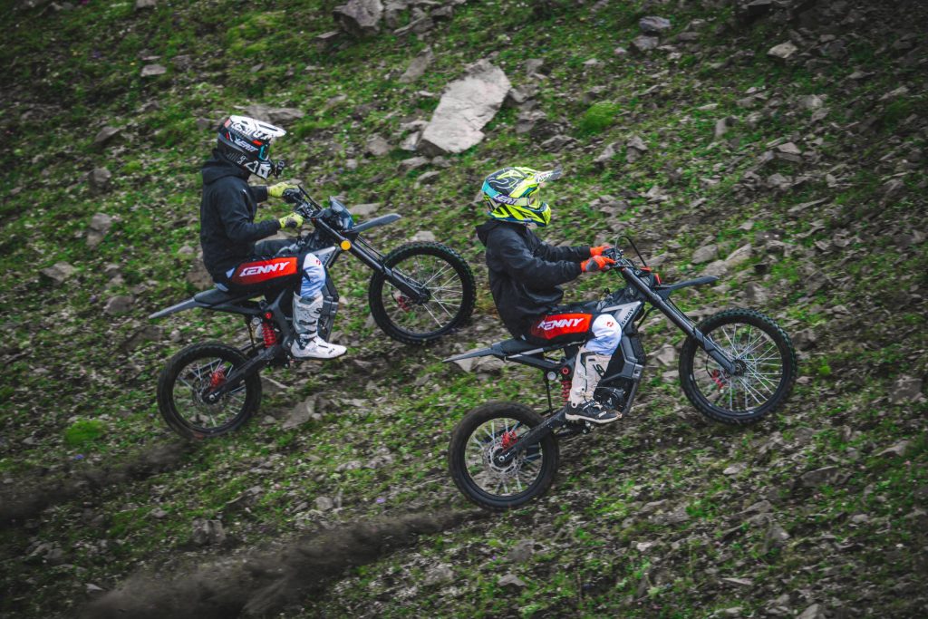 Two riders on Segway Xaber 300 electric dirt bikes on a grassy slope