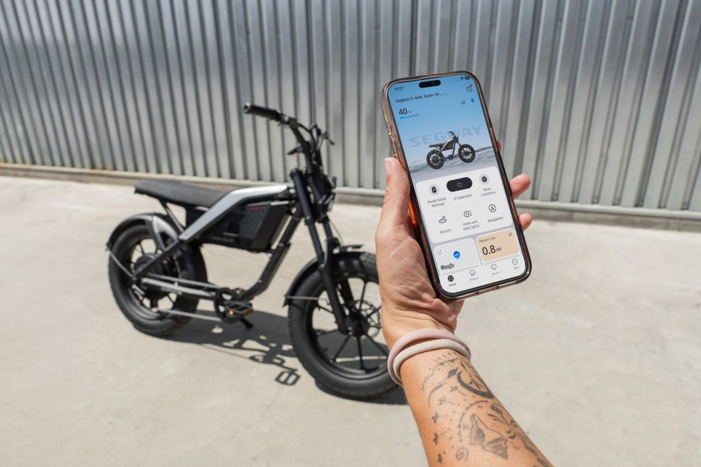 Rider holding the Segway Mobility app next to a Segway Xyber Air eBike